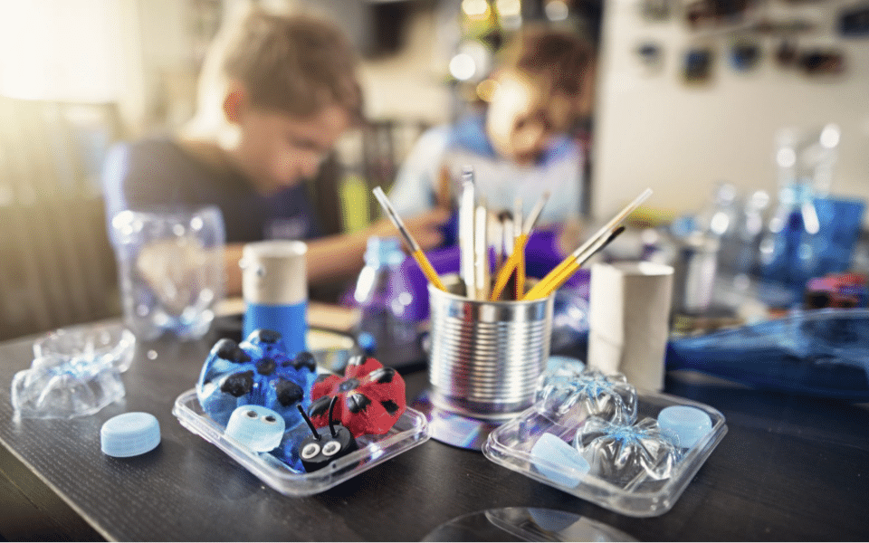 Close-up of different art supplies on a table with two children out of focus in the background.